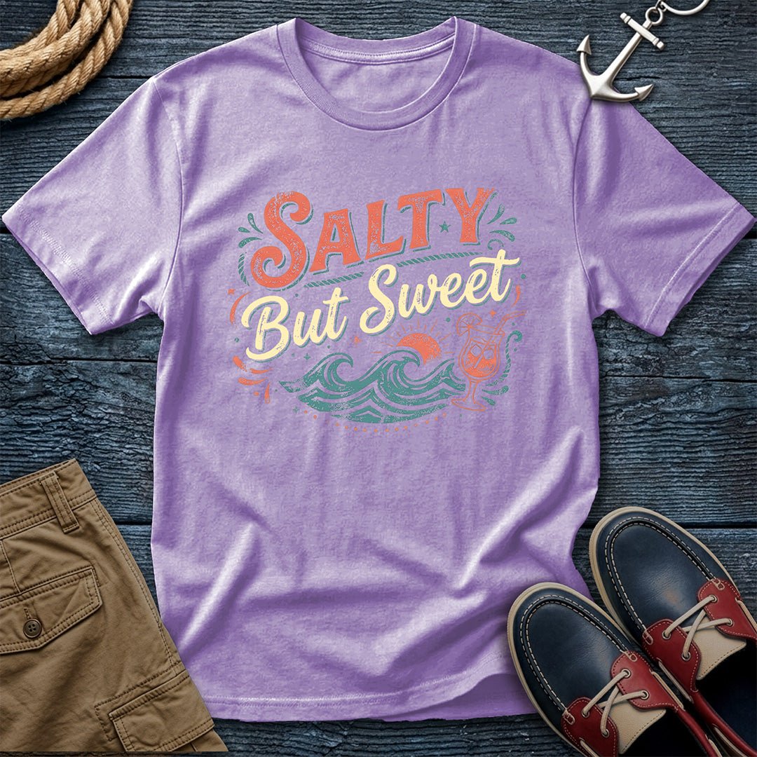 Purple t-shirt with 'Salty But Sweet' text and wave design on a wooden surface with shorts and shoes.