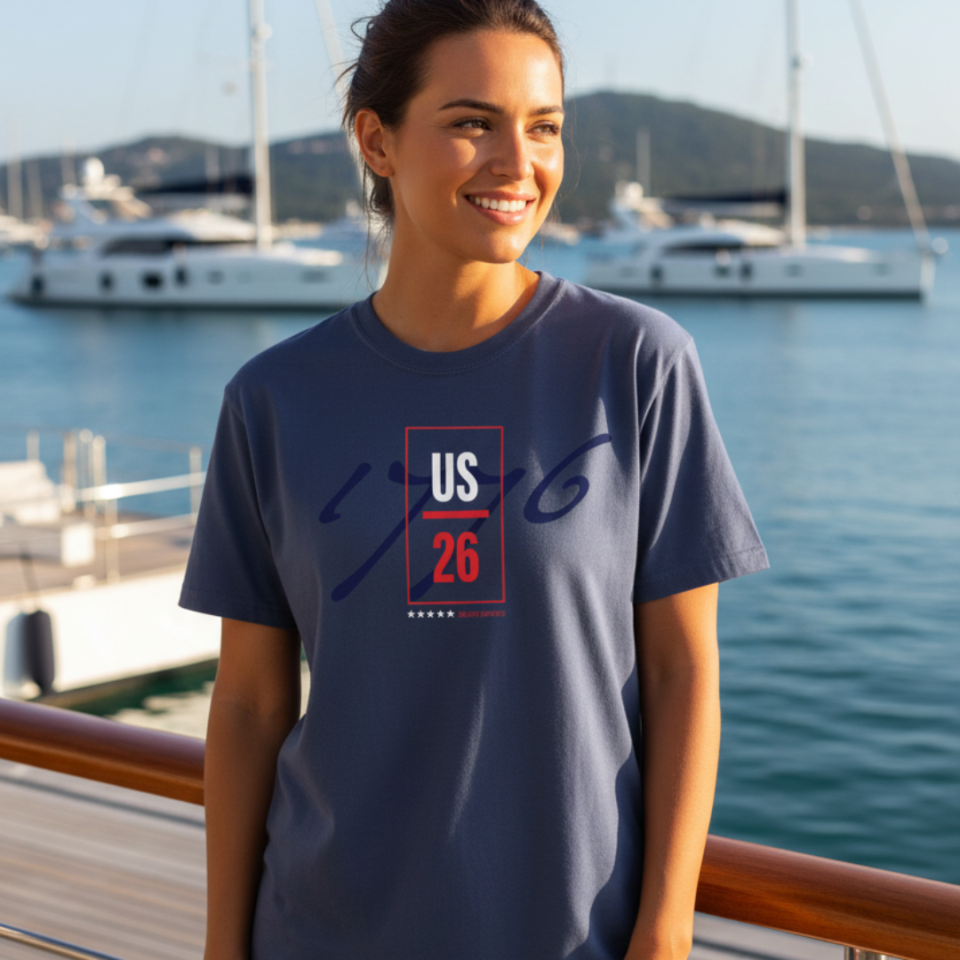 A woman wearing a Denim blue t-shirt with a red and white graphic print, standing on a wooden deck with a marina background of boats and water.