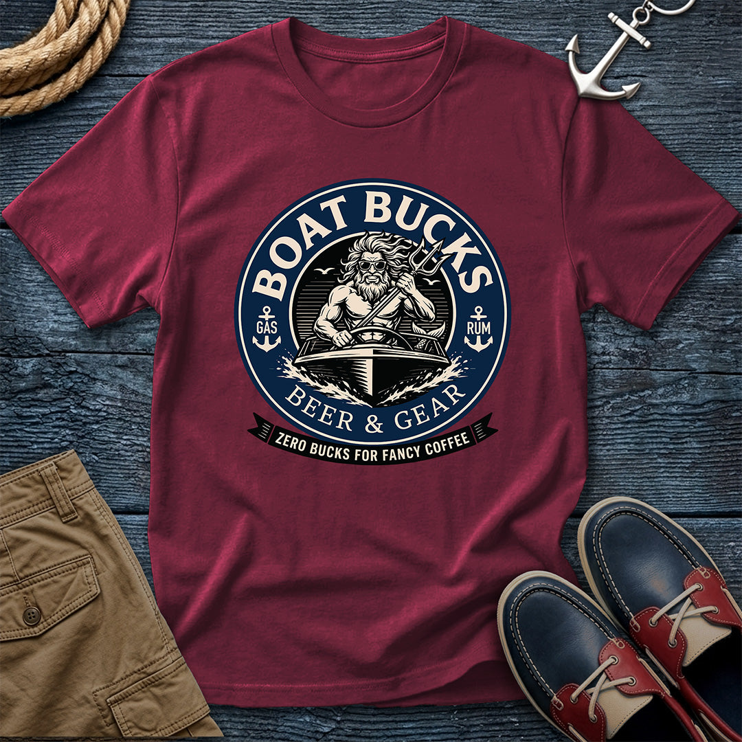 A Brick Colored short-sleeve graphic T-shirt laid flat on a dark blue wood surface, surrounded by nautical-themed props including rope, an anchor, khaki shorts, and navy-and-red boat shoes. The shirt features a large circular 'BOAT BUCKS BEER & GEAR' graphic with a sailor illustration and the tagline 'ZERO BUCKS FOR FANCY COFFEE.