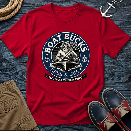 A red short-sleeve graphic T-shirt laid flat on a dark wood surface, styled with a rope, anchor, khaki shorts, and navy-and-red boat shoes. The shirt has a large circular nautical-style print reading “BOAT BUCKS BEER & GEAR” with an anchor, ship wheel, and banner reading “ZERO BUCKS FOR FANCY COFFEE.
