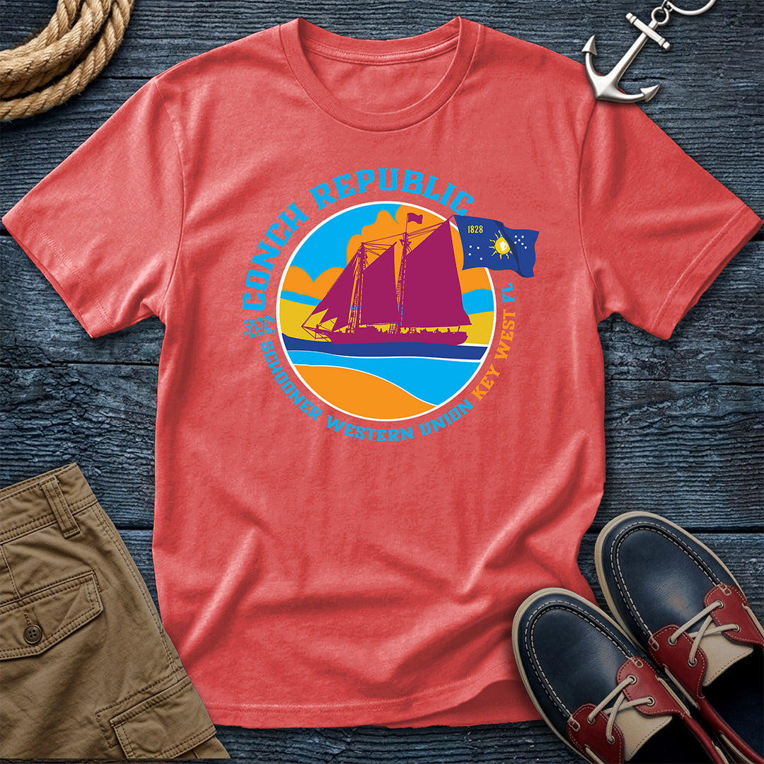 Conch Republic Key West Schooner Tee in Bright Salmon, Comfort Colors 1717, featuring a magenta schooner, blue Conch Republic flag, and orange sunset graphic, laid flat beside nautical accessories.