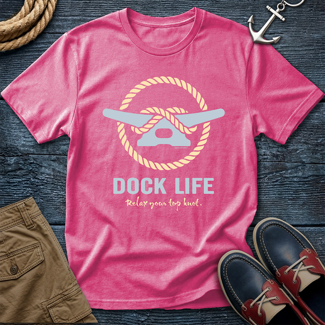 Pink t-shirt with 'Dock Life' graphic and text on a wooden surface with shorts and shoes.