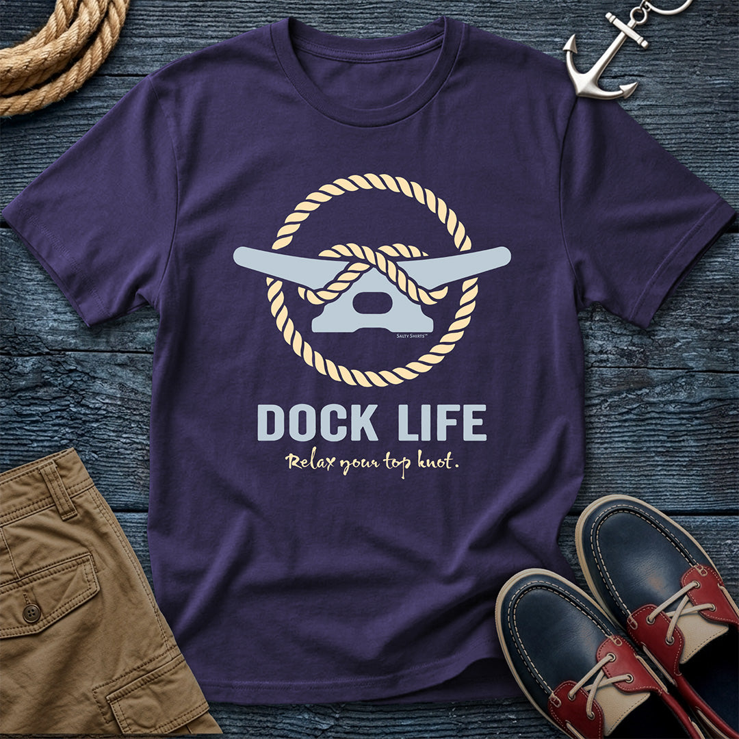 Purple t-shirt with 'Dock Life' graphic on a wooden surface with shorts and shoes.