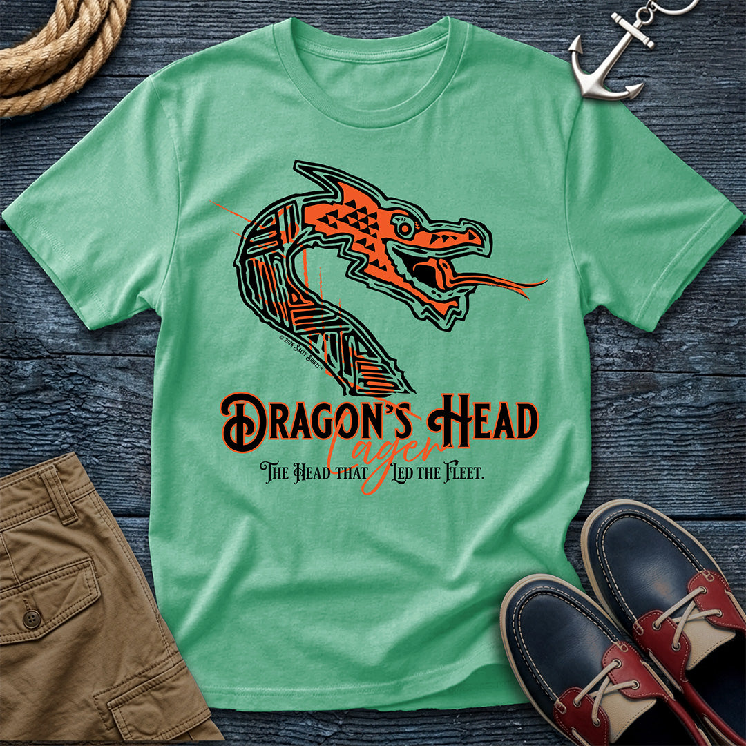 A mint green short-sleeve t-shirt with a graphic of a stylized orange and black dragon head and the text 'DRAGON'S HEAD' and 'The Head that Led the Fleet.' The shirt is laid flat on a dark wood surface with nautical props including an anchor, rope, tan shorts, and navy-and-red shoes.