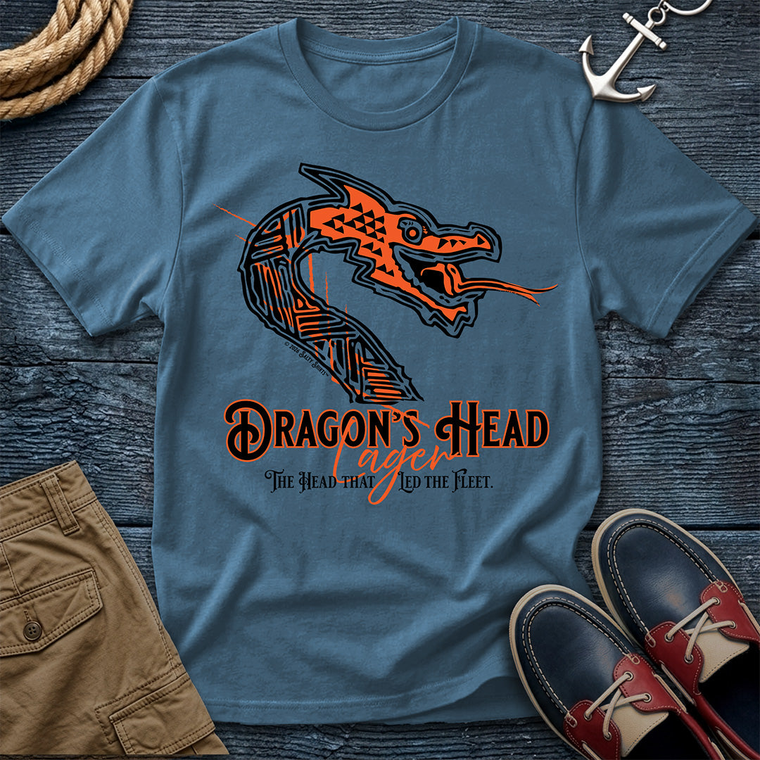 A blue crewneck t-shirt with a graphic of a stylized orange and black dragon head and the text 'DRAGON'S HEAD Lager: The Head That Led The Fleet', presented in a flat-lay arrangement with brown shorts, a rope, an anchor, and red-and-navy shoes on a dark wood background.