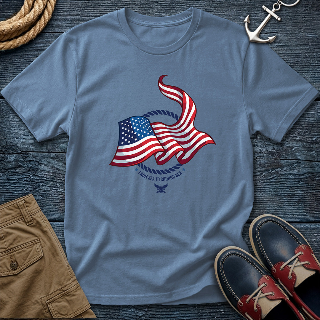 From Sea to Shining Sea American Flag Tee in Blue Jean, Comfort Colors 1717 garment-dyed shirt with a waving American flag inside a rope ring, curved text, and eagle-and-anchors mark