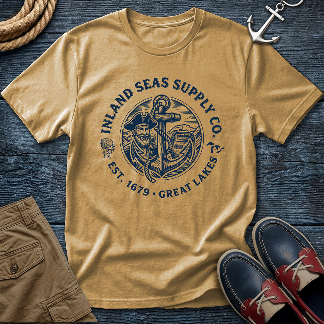 Mustard t-shirt with 'Inland Seas Supply Co' graphic on a wooden surface with shorts and shoes.