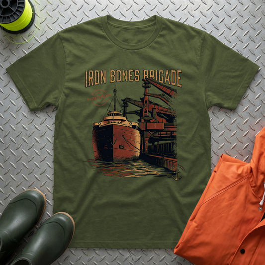 Green t-shirt with 'Iron Bones Brigade' design on a metal surface with shoes and an orange jacket.