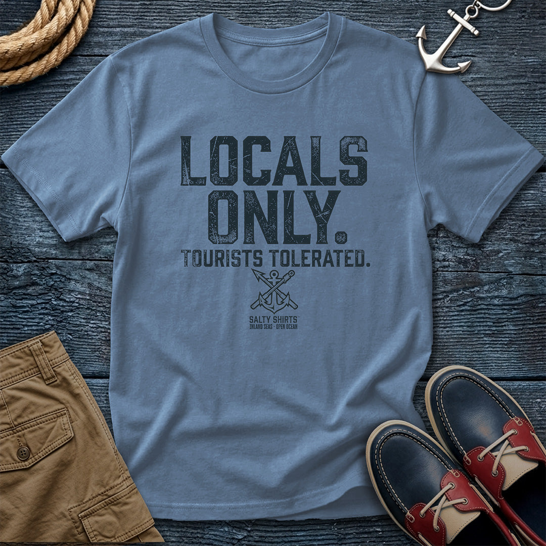 Blue t-shirt with 'Locals Only, Tourists Tolerated' text on a wooden surface with shorts and shoes.