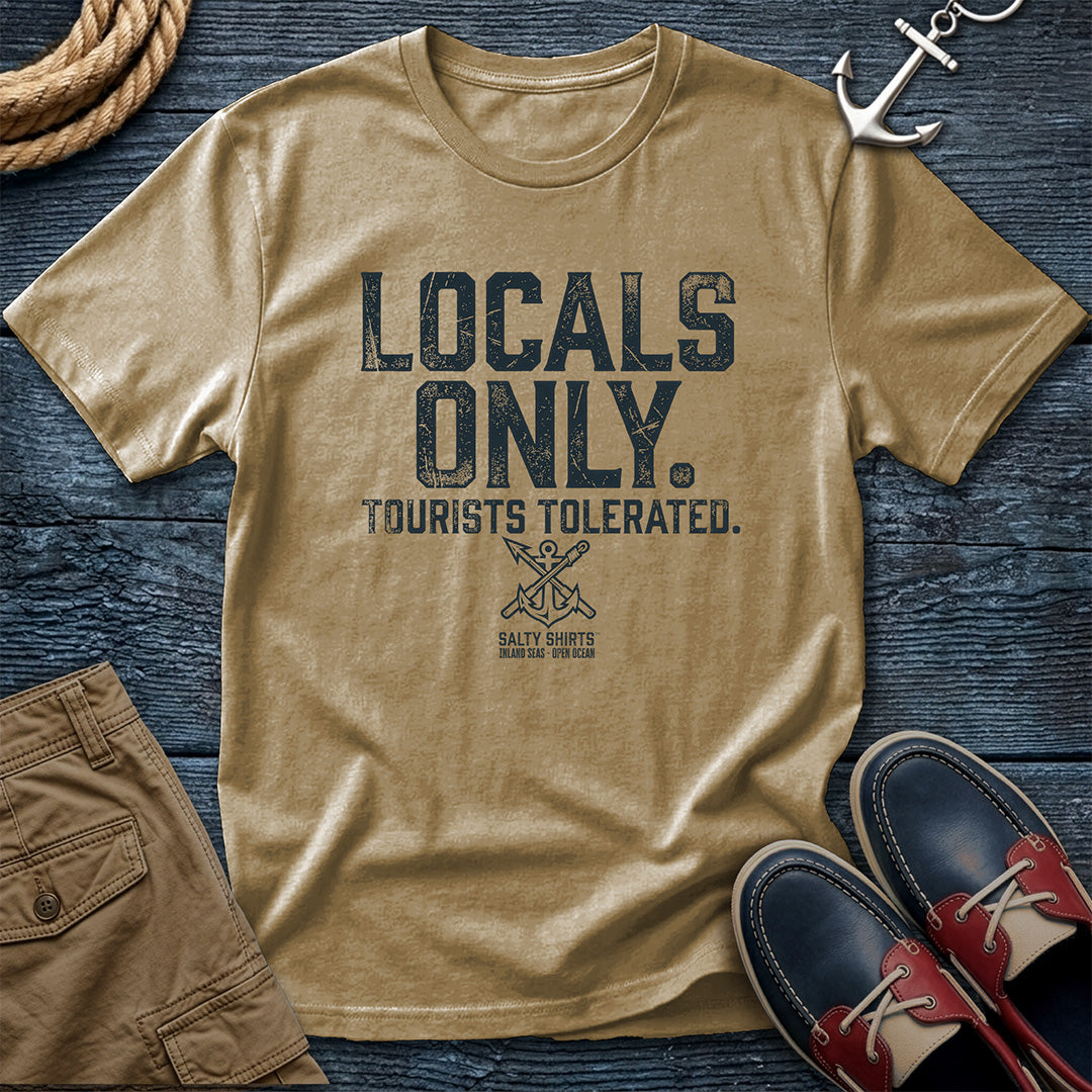 Khaki t-shirt with 'Locals Only, Tourists Tolerated' text on a wooden surface with accessories.