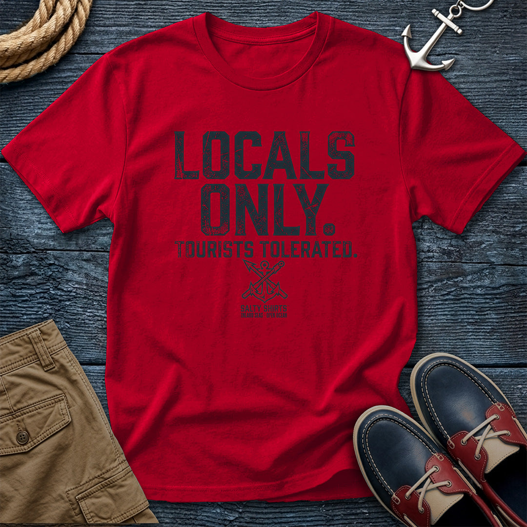 Red t-shirt with 'Locals Only, Tourists Tolerated' text on a wooden surface with accessories.