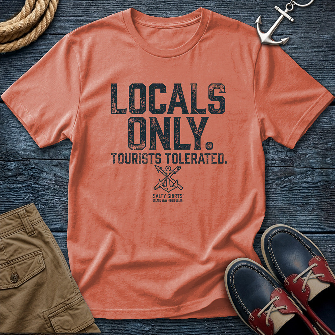 Teracota t-shirt with 'Locals Only, Tourists Tolerated' text on a wooden surface with shorts and shoes.