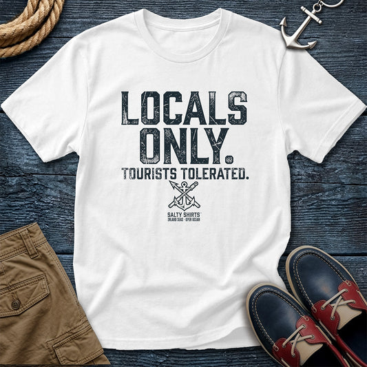 White t-shirt with 'Locals Only, Tourists Tolerated' text on a wooden surface with accessories.
