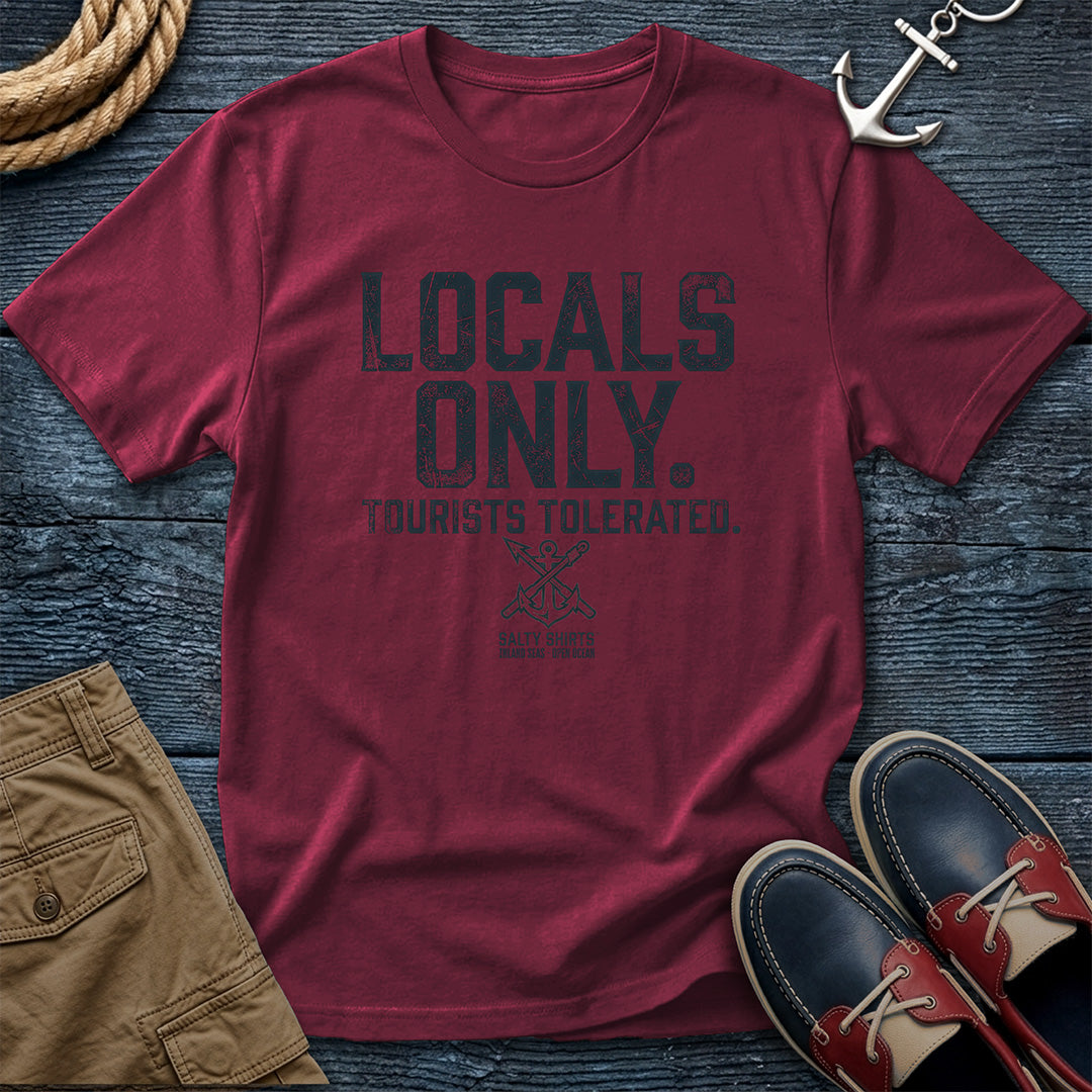 Brick t-shirt with 'Locals Only, Tourists Tolerated' text on a wooden surface with shorts and shoes.