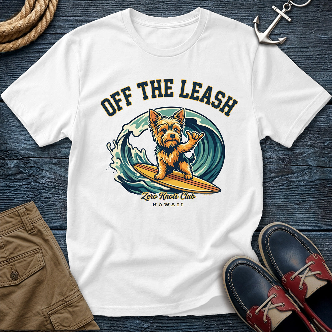 White t-shirt with a dog graphic and 'Off The Leash' text on a wooden surface with shoes and shorts.
