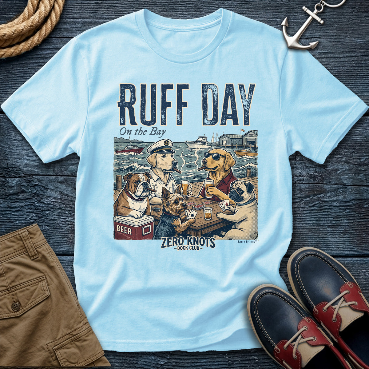 Light blue t-shirt with a graphic of dogs at a dock and 'Ruff Day on the Bay' text, displayed with shorts and shoes on a wooden dock.
