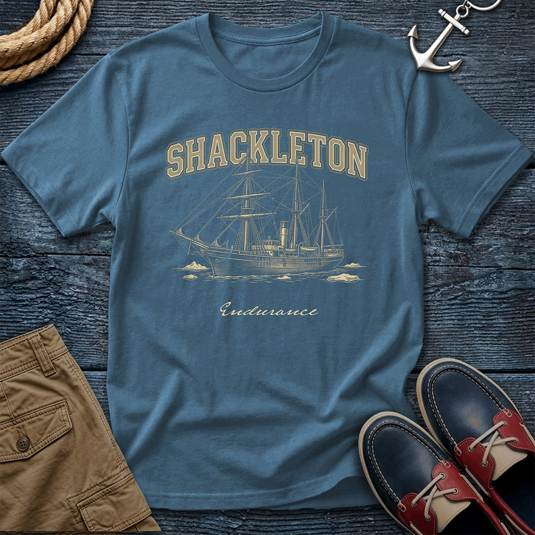 Blue t-shirt with Shackleton Endurance design on a wooden surface with shorts and shoes.