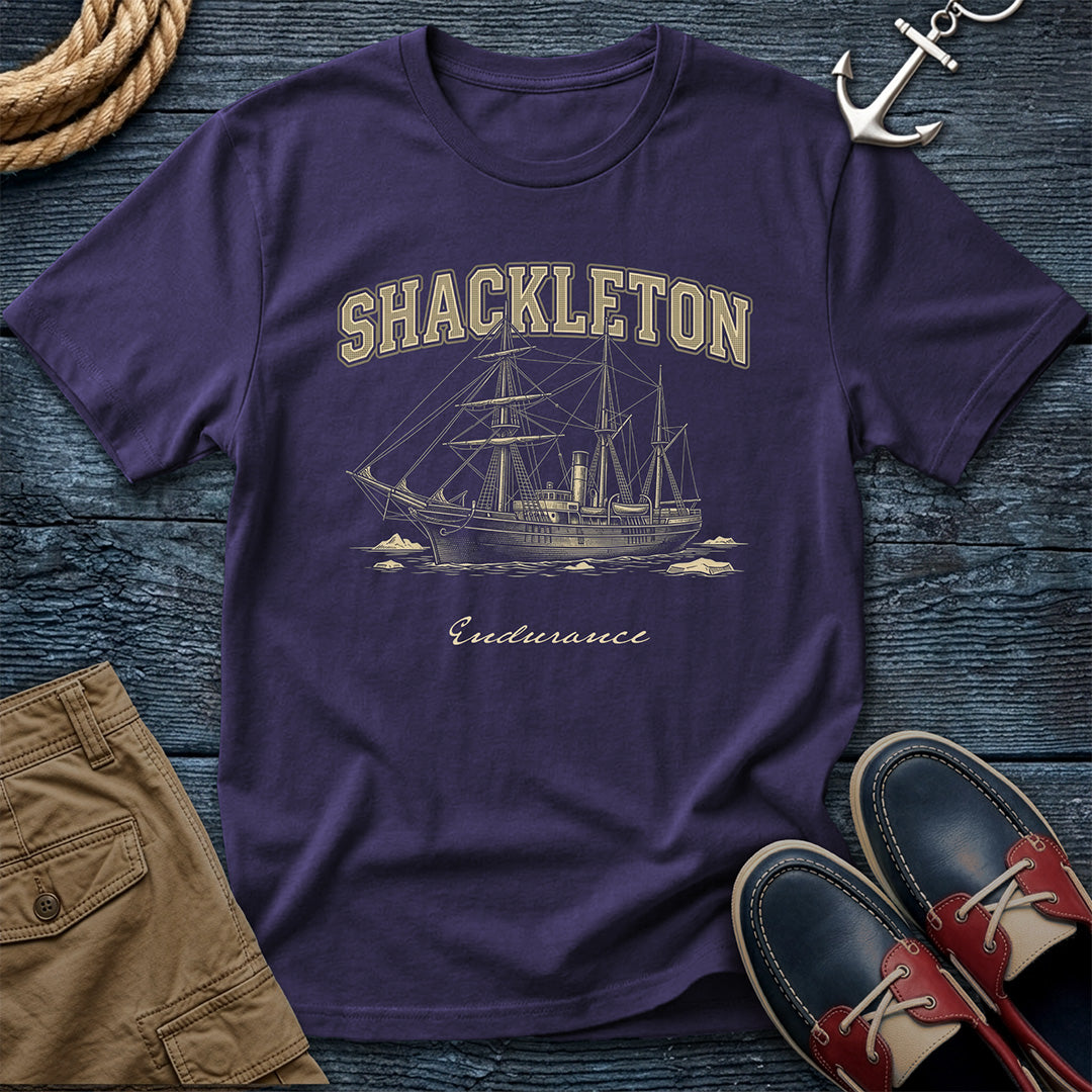 Purple t-shirt with 'Shackleton Endurance' design on a wooden surface with shorts and shoes.