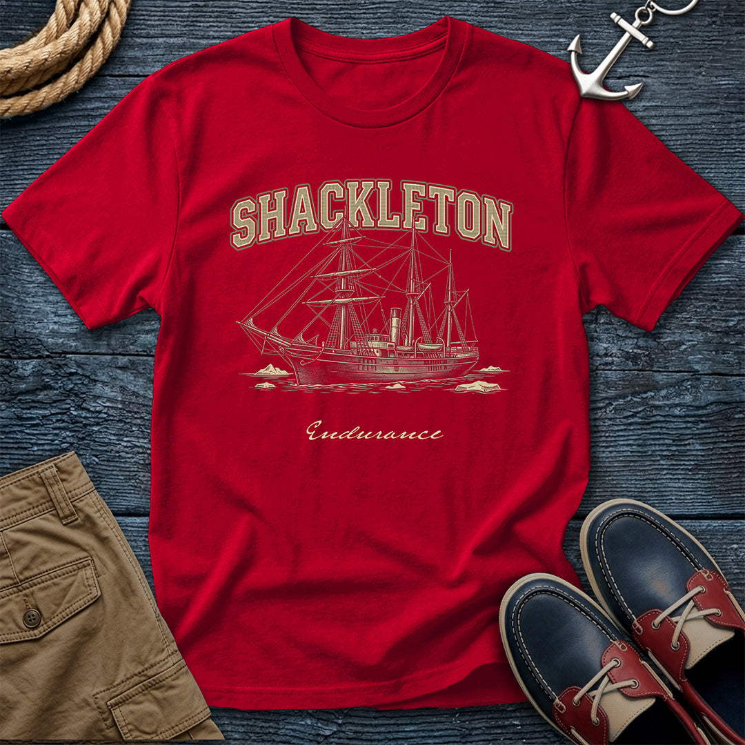 Red t-shirt with Shackleton Endurance design on a wooden surface with shorts and shoes.