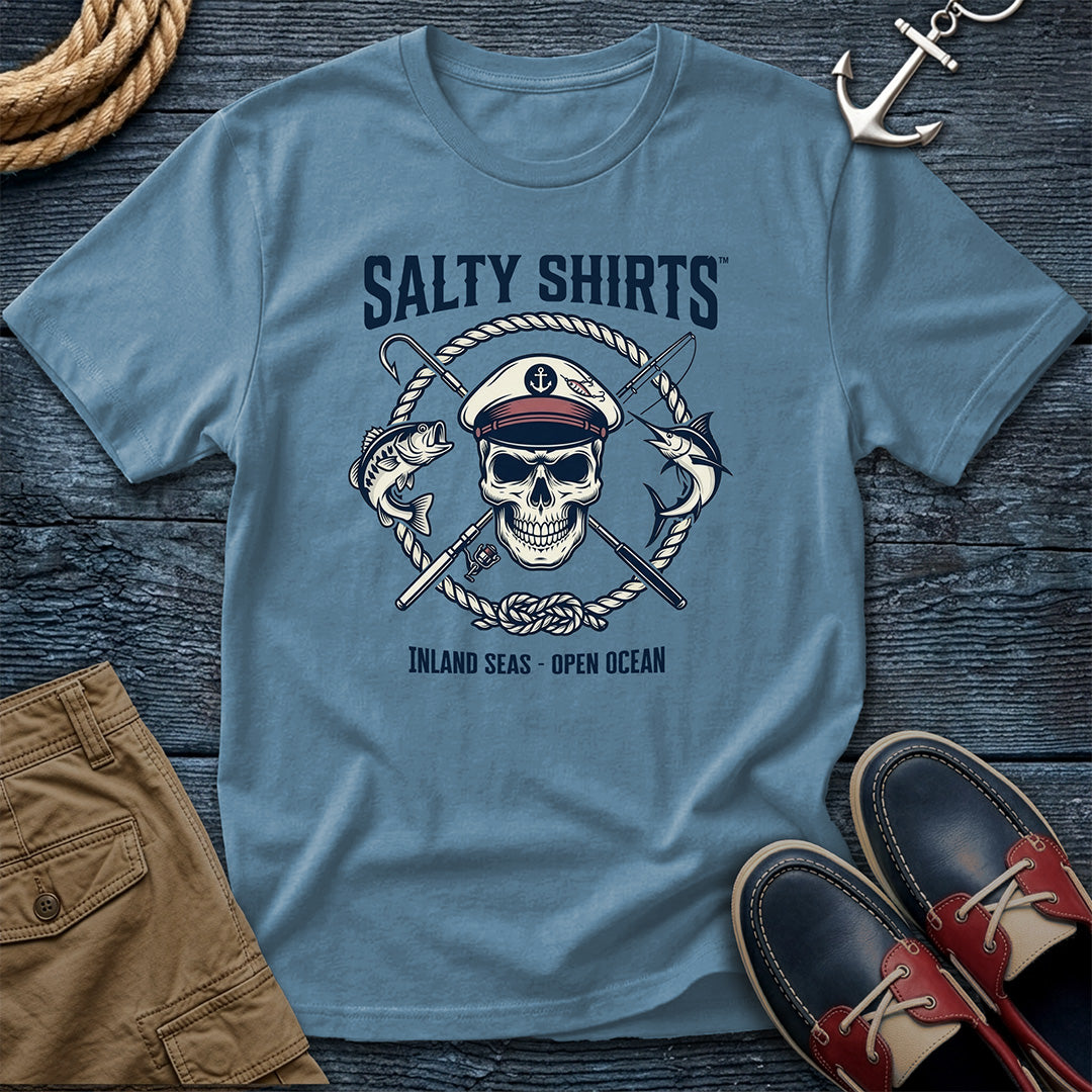 Blue t-shirt with skull and crossed swords design on a wooden surface with shorts and shoes.