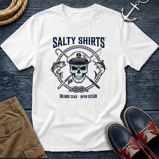 White t-shirt with skull and crossed swords design on a wooden surface with shoes and shorts.