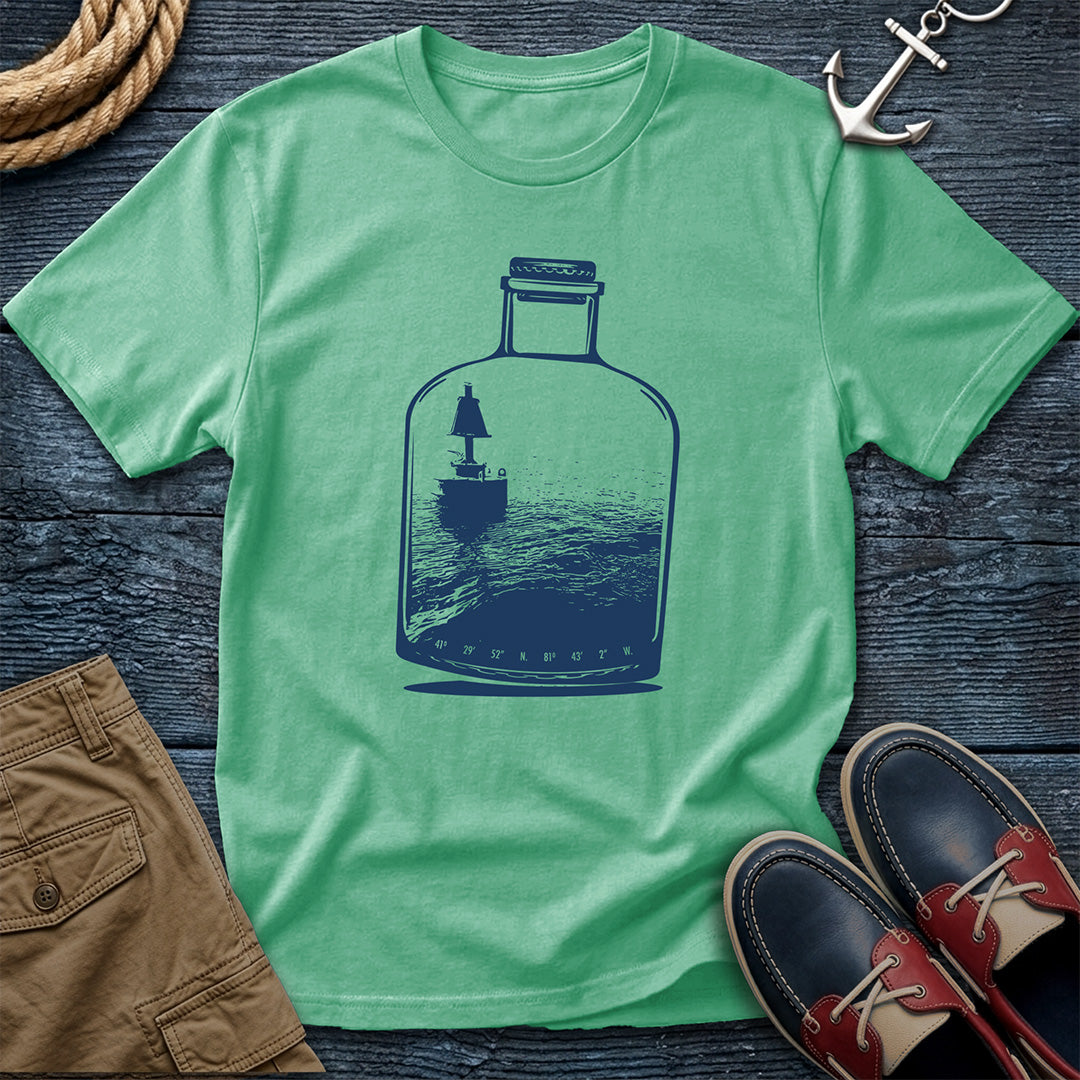 Green t-shirt with a Channel Marker in a bottle graphic on a wooden surface with shoes and shorts.