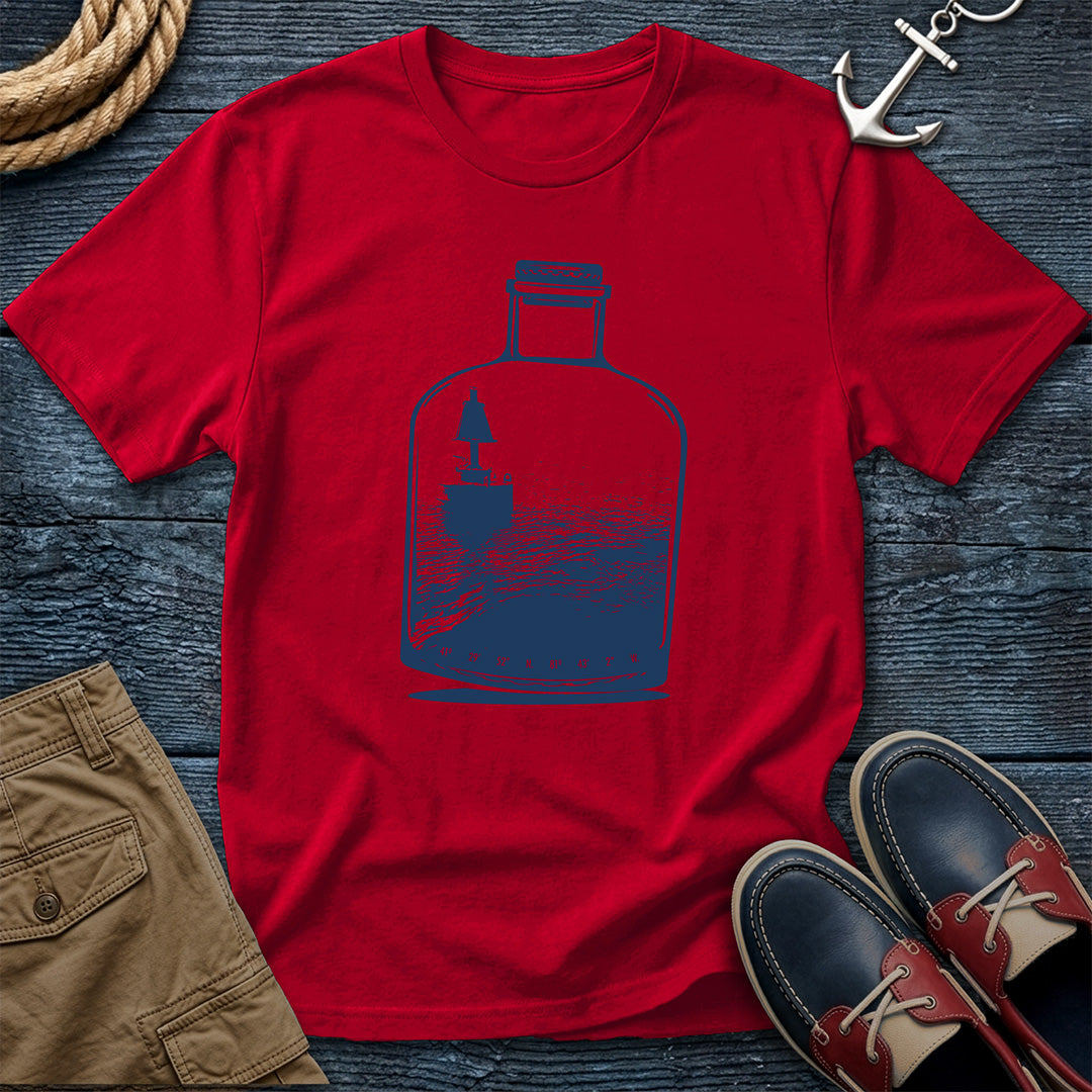 Red t-shirt with a blue bottle graphic on a wooden surface with shoes and shorts.