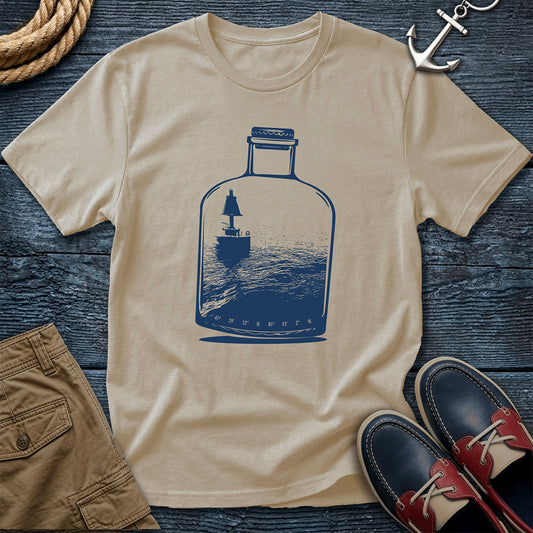 Sand t-shirt with a blue bottle graphic on a wooden surface with shorts and shoes.