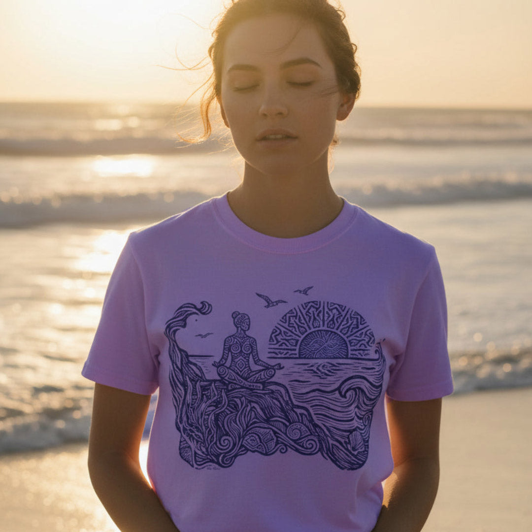 Sunrise Shore Meditation Tee in Orchid, Comfort Colors 1717 garment-dyed shirt with a seated shoreline figure, rising sun, geometric mandala, waves, shells, kelp, and circling gulls.